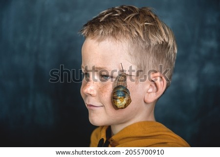 Young boy with snail on face. Focus on snail. Animal pet. School kid playing. Child love nature.