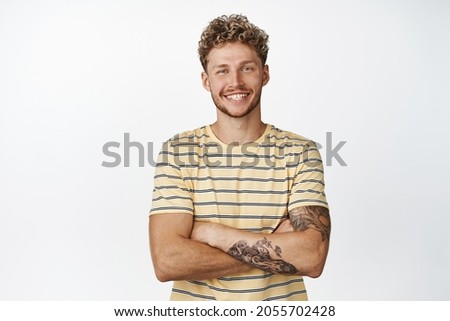 Handsome blond young man with moustache, looking confident and professional, cross arms on chest, smiling with white healthy smile, standing over white background