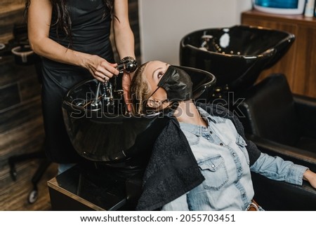 Beautiful middle-aged woman with protective face mask in hair salon.