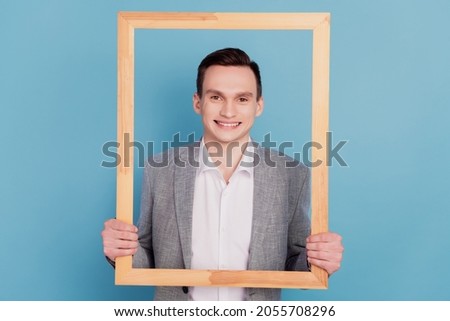 Portrait of funky cheerful handsome man hold wooden frame make picture isolated over blue color background