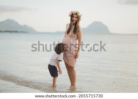 A handsome boy kisses his pregnant mother's belly on the island.