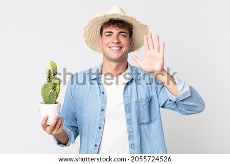 young handsome man smiling and looking friendly, showing number five. farmer holding a decorative cactus