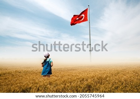 Adorable baby girl is in a field with fog and looking to Turkish national flag admiringly.