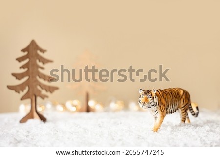 Figurine of tiger, wooden fir trees in snow on beige background. Tiger symbol of the Chinese new year 2022. Christmas greeting card. Copy space