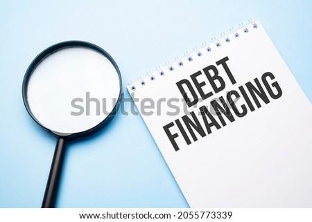 Magnifying glass loupe with sign Debt financing blue table.