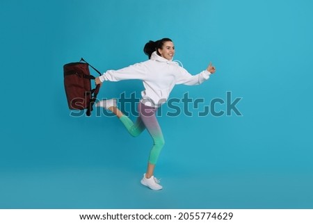 Beautiful woman with sports bag running on light blue background