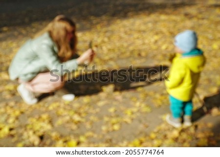 Blurred, defocused photograph of a young girl taking pictures of her son in an autumn park