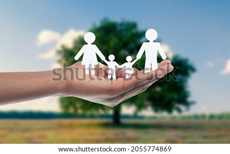 Female european hand holds silhouettes of people, mom dad and children on nature with blue sky and green grass background. Caring for planet, recycling, ecology and environment, protecting family