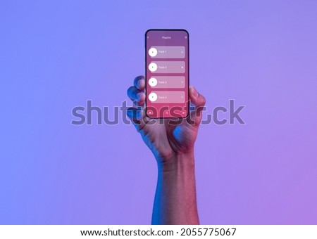 Black Male Hand Holding Smartphone With Opened Audio Player Interface, Unrecognizable African American Man Enjoying New Music App, Standing Under Neon Light Over Purple Background, Collage Royalty-Free Stock Photo #2055775067