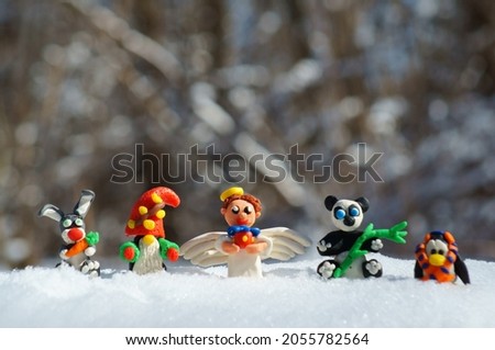 Figurines of fairy-tale characters in the winter forest. An angel with a gift, a dwarf, a rabbit with a carrot, a panda, a penguin in a scarf.