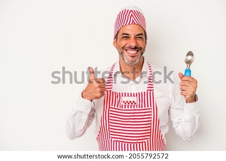 Middle age caucasian ice maker caucasian man holding a spoon isolated on white background  smiling and raising thumb up