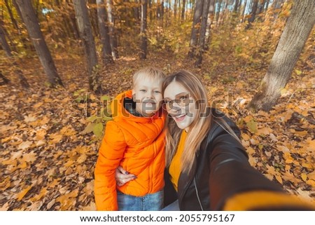 Son and mother are taking selfie on camera in autumn park. Single parent, leisure and fall season concept.