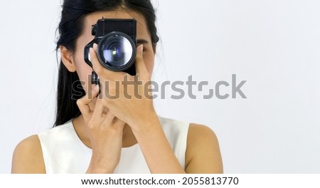 Young asian woman in white dress looking through the viewfinder while shooting with the camera.