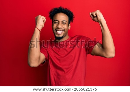 Young african american man with beard wearing casual red t shirt celebrating surprised and amazed for success with arms raised and open eyes. winner concept. 