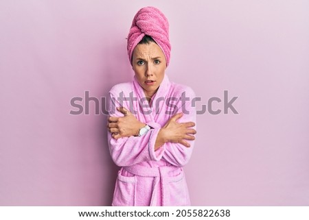 Young blonde woman wearing shower towel cap and bathrobe shaking and freezing for winter cold with sad and shock expression on face  Royalty-Free Stock Photo #2055822638