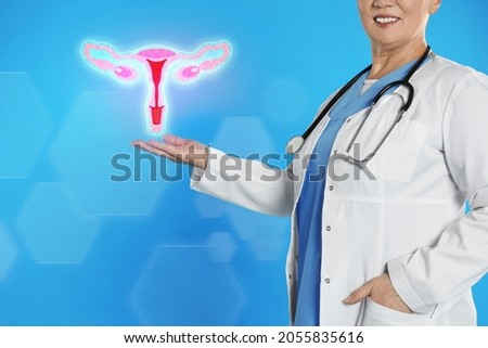 Mature doctor demonstrating virtual icon with illustration of female reproductive system on light blue background, closeup. Gynecological care 