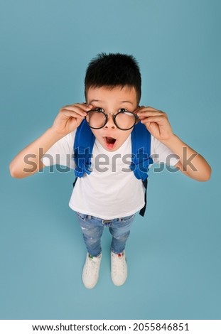 Funny Asian Schoolboy With Backpack Adjusting Glasses And Looking At Camera With Excitement, Surprised Korean Male Pupil Child Standing With Opened Mouth Over Blue Background, Above View