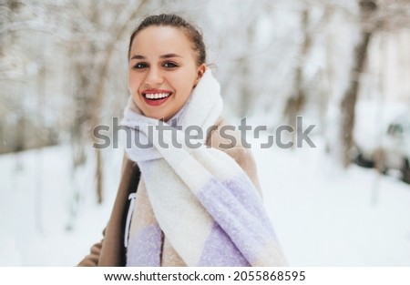 Closeup photo of beautiful brunette female with sharp look, half of young woman face covered with light colored knitted scarf, girl looking into camera with dark brown eyes with black eyeliner makeup
