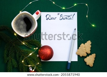 Christmas wishlist 2022 or letter to Santa on green colored paper background. Festive decoration, Christmas garland, Christmas tree branch. Flat lay. View from above.