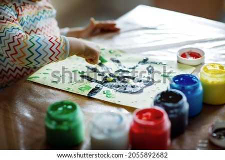 Closeup of little creative toddler girl painting with finger colors an owl bird. Child having fun with drawing at home, in kindergaten or preschool. Games, education and distance learning for kids.
