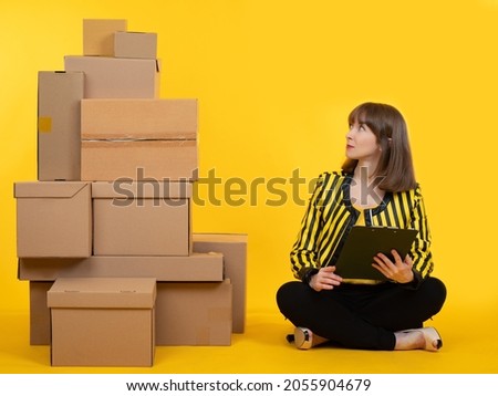 Small or home business concept. Woman next to boxes as symbols of small business. Woman owns her own online store. Girl in bright clothes is engaged in business. Businesswoman on yellow background