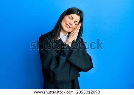 Young hispanic woman wearing judge uniform sleeping tired dreaming and posing with hands together while smiling with closed eyes. 