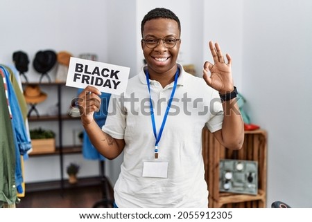 Young african man holding black friday banner at retail shop doing ok sign with fingers, smiling friendly gesturing excellent symbol 
