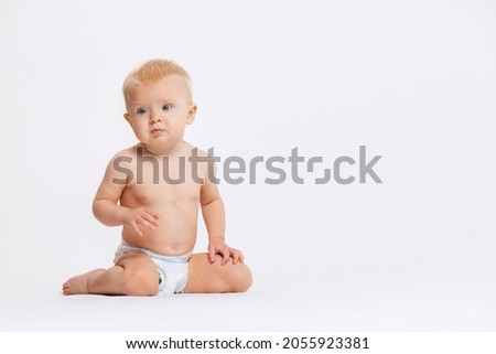 Portrait of little cute toddler girl, baby calmly sitting in diaper isolated over white studio background. Concept of childhood, motherhood, life, birth, family, happiness. Copy space for ad