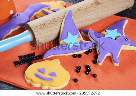 Happy Halloween orange and purple sugar cookies in cat, hat, bat and pumpkin shapes with rolling pin and decorations - close up.