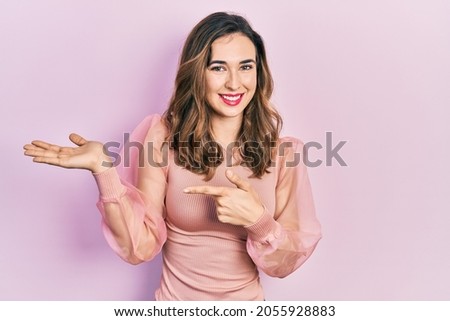 Young hispanic girl wearing casual clothes amazed and smiling to the camera while presenting with hand and pointing with finger. 