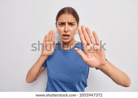 Do not come closer. Displeased woman shows her denial opinion says stay away from me calm down or slow asks to keep distance demonstrates taboo gesture dressed casually isolated over white wall Royalty-Free Stock Photo #2055947372