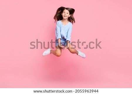 Photo of cute charming schoolgirl wear blue outfit jumping high smiling isolated pink color background