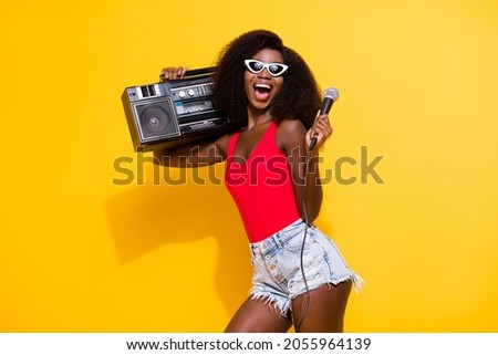 Portrait of attractive trendy cheerful ecstatic girl carrying boombox singing having fun isolated over bright yellow color background