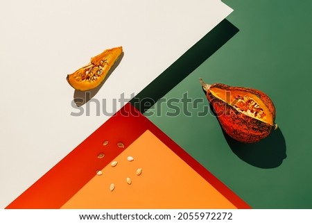 Geometric fall composition with pumpkins and seeds on tri tone green, orange and orange background. Creative vegetable food concept. Modern Thanksgiving or Halloween idea. Minimal pop art backdrop.