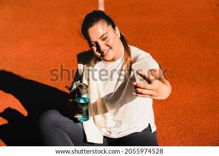 Close up portrait of a plump plus-size fat sporty athlete relaxing after jogging running workout yoga class taking selfie photo on smart phone for social media, having video call outdoors in park