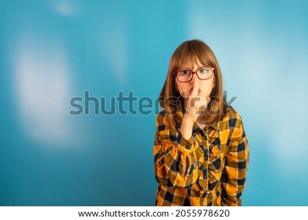 Cute little girl doing silence sign the finger near lips over blue background, sign and gesture concept blue pastel background copy-space.