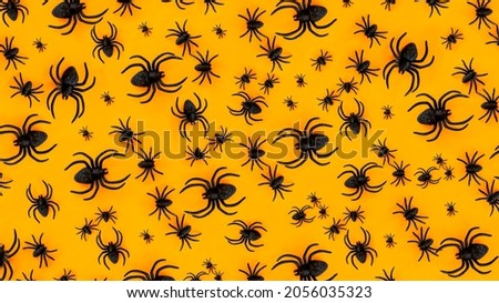 Flat lay pattern banner of black horror spiders of different sizes directed in different directions on orange backdrop with copy space. Halloween decoration spooky background concept for holidays.