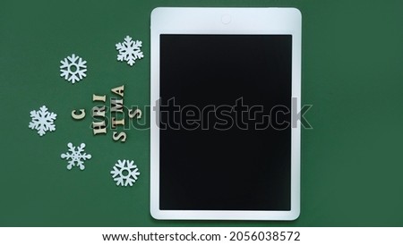 creative Christmas tree made of letters and the inscription "Christmas" on a green background surrounded by snowflakes with a place for text and a mockup tablet, the concept of Christmas and new year