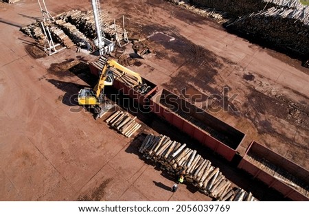 Excavator with log grab crane unloads timber from freight car. Crane with claw loads logs onto log train for lumber mill. Illegal logging and timber export. Wood Machine and Log Grabbing. Royalty-Free Stock Photo #2056039769