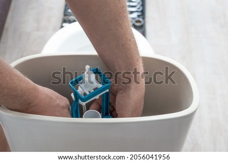 Plumbing installation. The plumber installs a flush pump in the toilet cistern. Royalty-Free Stock Photo #2056041956