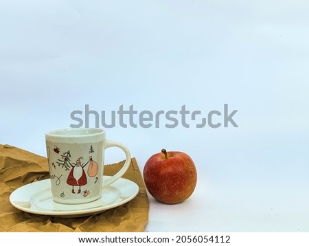 A cup with Santa Claus picture on the craft paper and red apple on white background with area place for text 