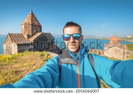 Man solo traveler takes selfie photo against the background of Sevanavank monastery at the Sevan lake. Vacation in Armenia concept