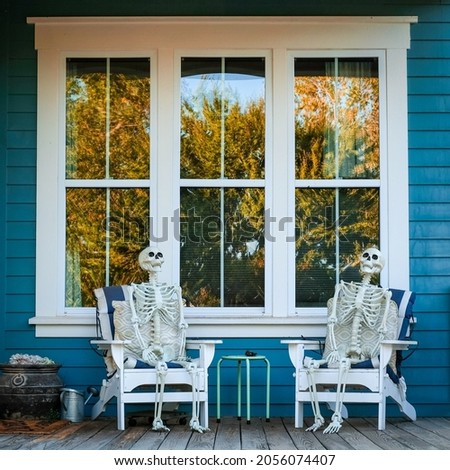 Skeletons sitting in chairs on porch for halloween