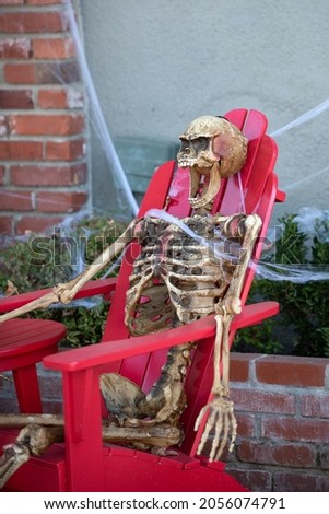 Happy skeleton relaxes in a chair. Scenery for Halloween in October. Decoration in the yard