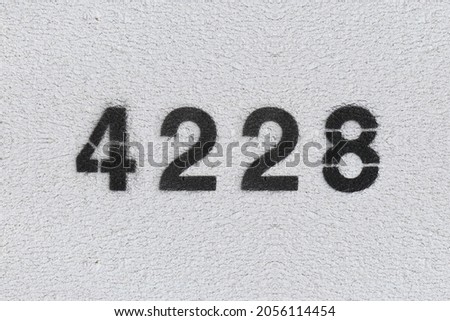 Black Number 4228 on the white wall. Spray paint. Number four thousand two hundred and twenty eight.