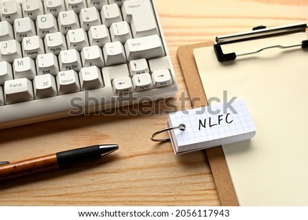 There is a word book with the word of NLFC which is an abbreviation for National Life Finance Corporation on the desk with a pen and a keyboard.