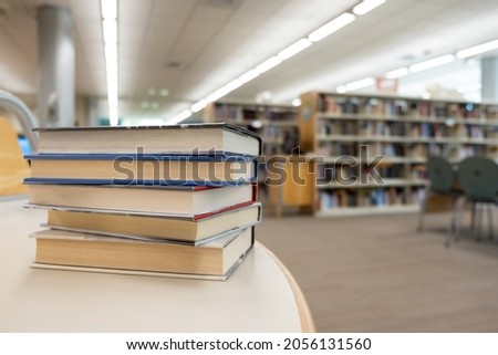 Stack of books on table against bookshelf at library for education, literature or wisdom concept