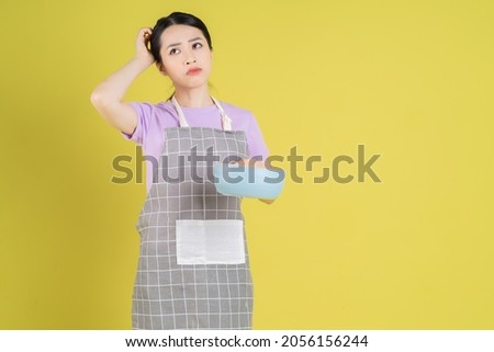 Young Asian housewife posing on yellow background Royalty-Free Stock Photo #2056156244