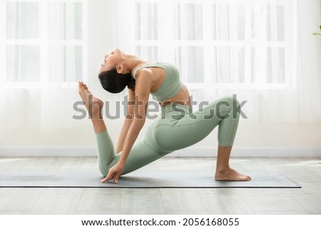 Side view of Asian woman wearing green sportwear doing Yoga exercise,Yoga One Legged King Pigeon pose or Eka Pada Rajakapotasana,Calm of healthy young woman breathing and meditation with yoga at home Royalty-Free Stock Photo #2056168055