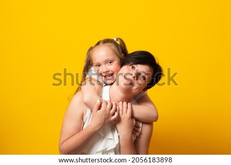 Happy woman, have fun with cute child baby girl 6-7 years old Mommy little kid daughter stand behind hug, isolated on yellow background. Mother's Day love family concept.